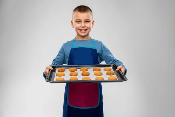 Fiú kötényben tartja sütő tálca sütemények — Stock Fotó