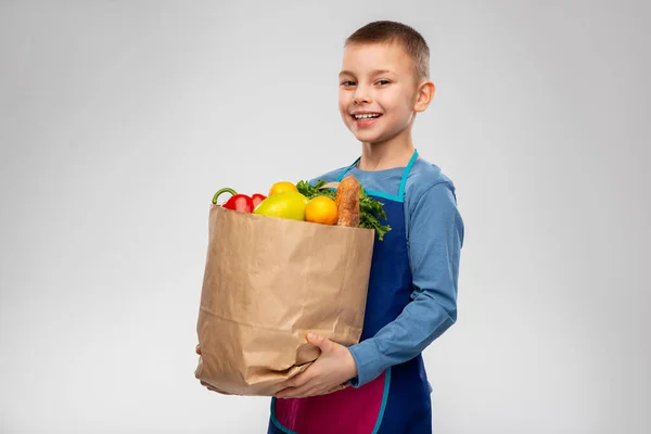 Ragazzo sorridente in grembiule contenente sacchetto di carta con cibo — Foto Stock