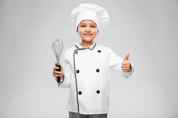 Dívka v kuchaři toque s whisk ukazující palce nahoru — Stock fotografie
