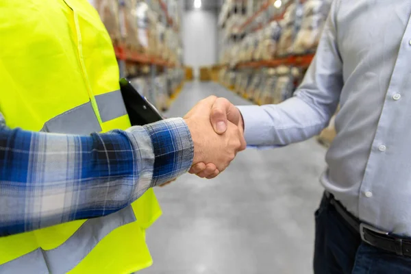 Arbeider en zakenman schudden handen in magazijn — Stockfoto