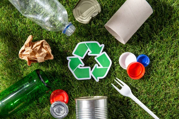 Green recycle sign with household waste on grass — Stock Photo, Image