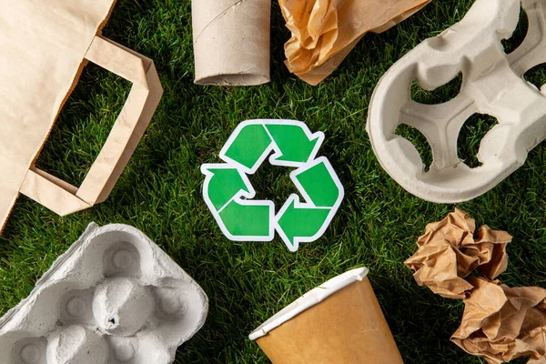Sinal de reciclagem verde e resíduos de papel na grama — Fotografia de Stock