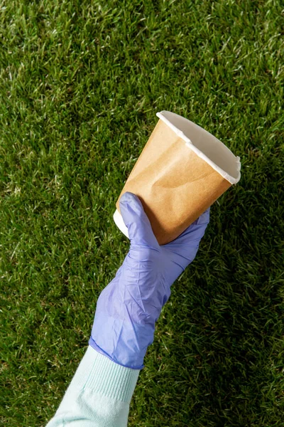 Közelről kéz a kézben a kesztyűben kávéscsészével a fűben — Stock Fotó