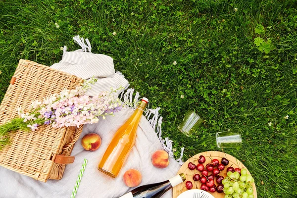 Comida, bebidas y cesta en la manta de picnic en la hierba — Foto de Stock