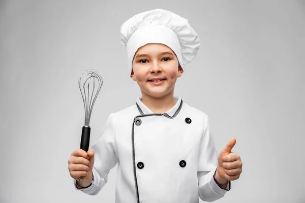 Chlapec v kuchařské toque s whisk ukazující palce nahoru — Stock fotografie