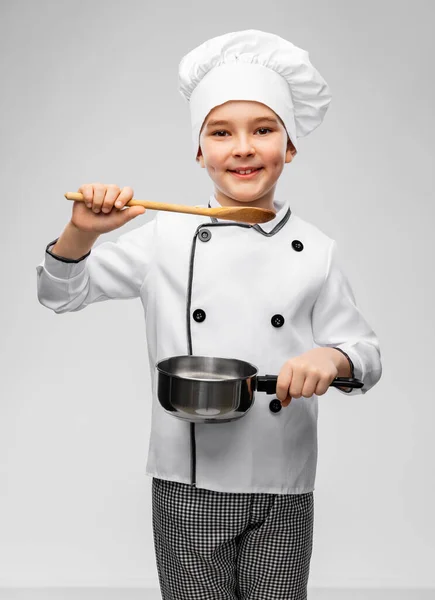 Boy in chefs toque with saucepan cooking food — Stock Photo, Image