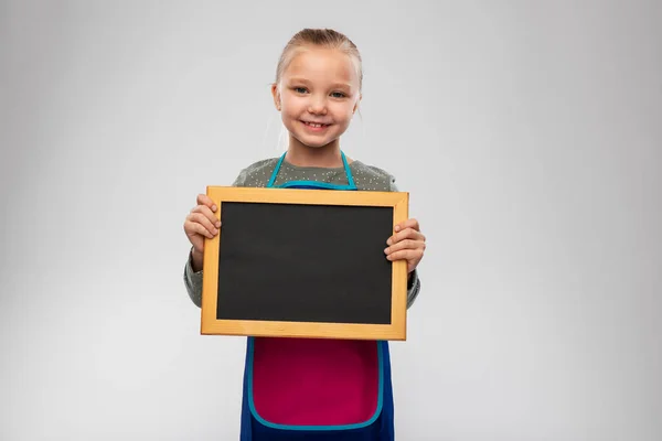 Usmívající se holčička v zástěře drží tabuli — Stock fotografie