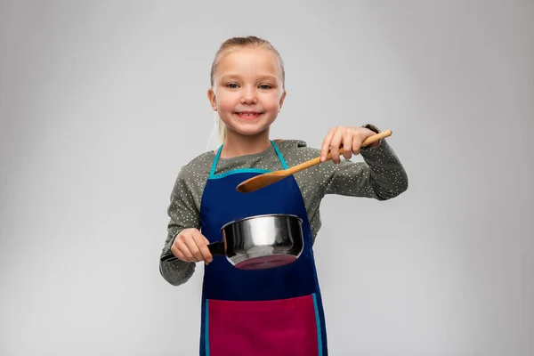 Önlüklü küçük kız tencereyle yemek pişiriyor. — Stok fotoğraf