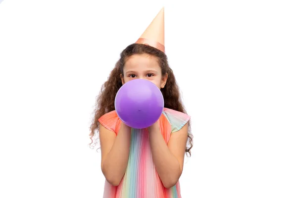 Liten flicka i födelsedagskalas hatt blåser ballong — Stockfoto