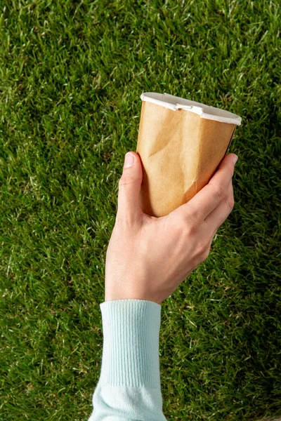 Close up of hand picking coffee cup from grass — Stock Photo, Image