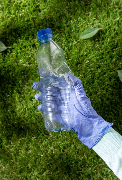 Mano nel guanto raccogliendo bottiglia di plastica da erba Immagine Stock