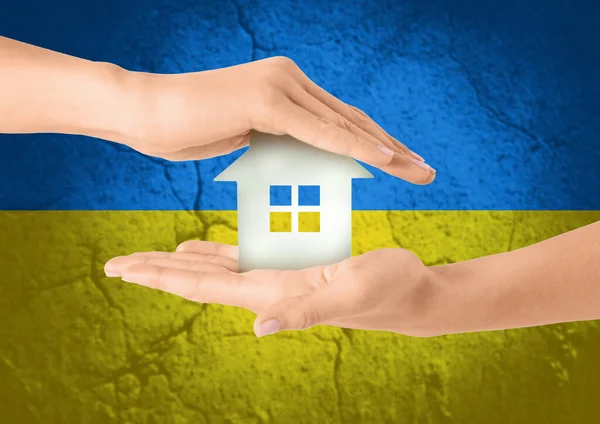 Руки тримають будинок над прапором українських кольорів — стокове фото