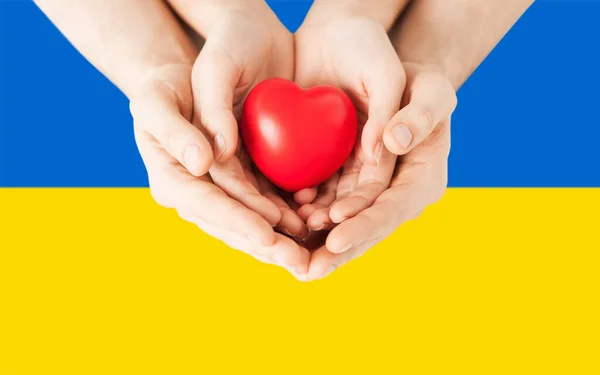 Hands holding red heart shape over flag of ukraine — Stock Photo, Image