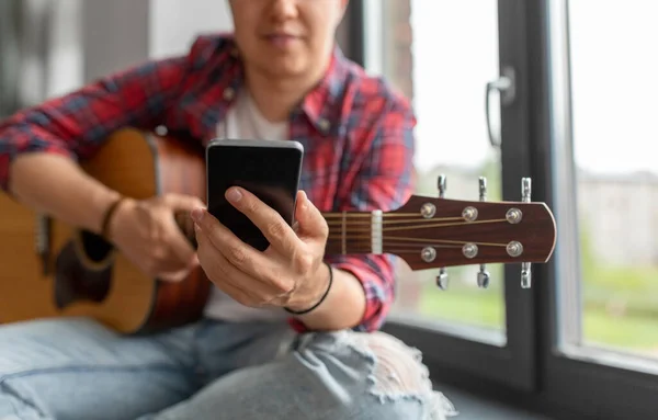 man with guitar and phone sitting on sill