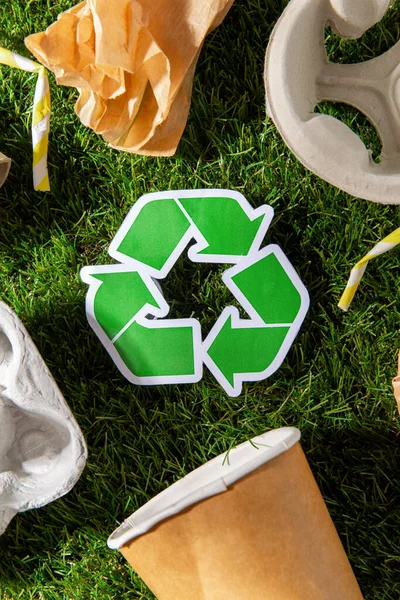 Green recycling sign and paper waste on grass — Stock Photo, Image