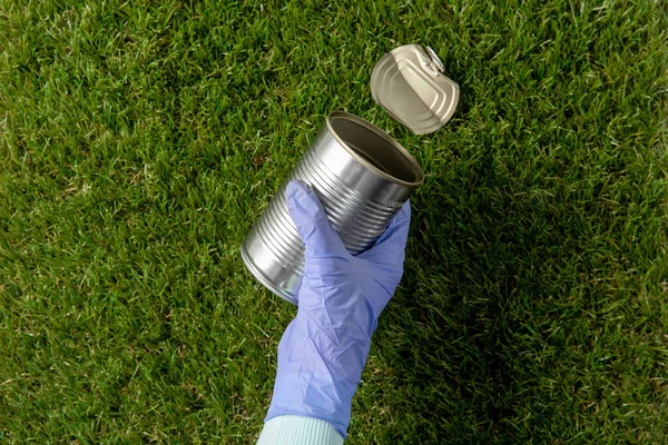Close up of hand in glove with used can on grass — 图库照片