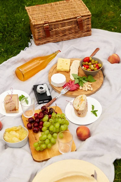 Comida, bebidas e cesta de piquenique em cobertor na grama — Fotografia de Stock