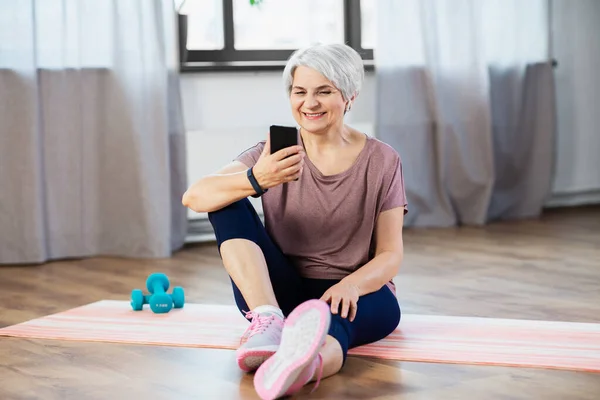 Mulher idosa com smartphone exercitando em casa — Fotografia de Stock