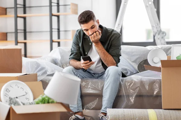 Hombre triste con teléfono inteligente y cajas de mudanza a casa —  Fotos de Stock