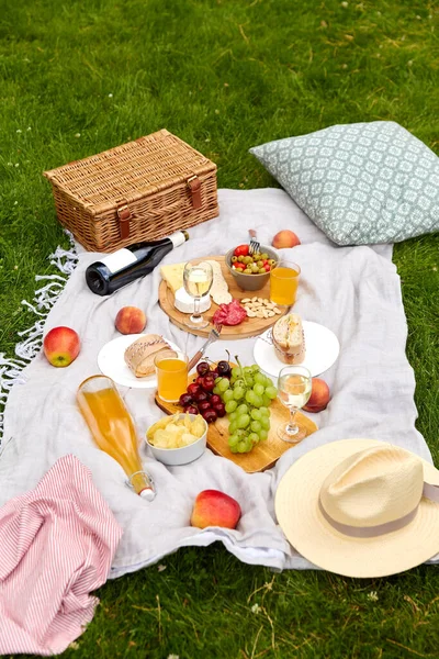 Jídlo, nápoje a piknikový koš na dece na trávě — Stock fotografie