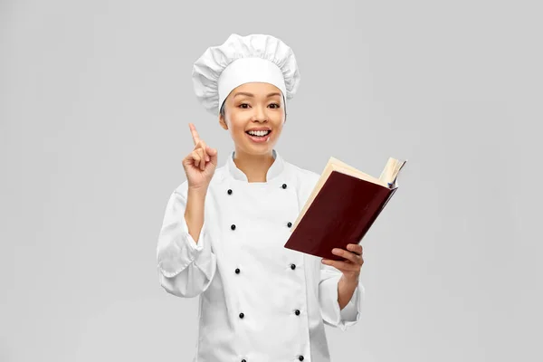 Kucharka z książką kucharską wskazującą palcem w górę — Zdjęcie stockowe