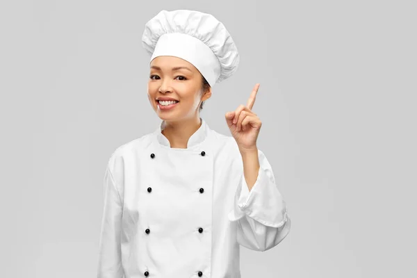 Glimlachende vrouwelijke chef-kok in jasje wijzende vinger omhoog — Stockfoto