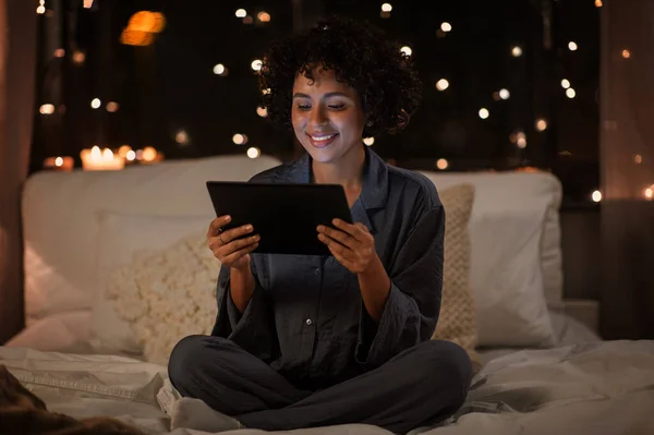 Mujer feliz con la tableta pc sentado en la cama por la noche —  Fotos de Stock