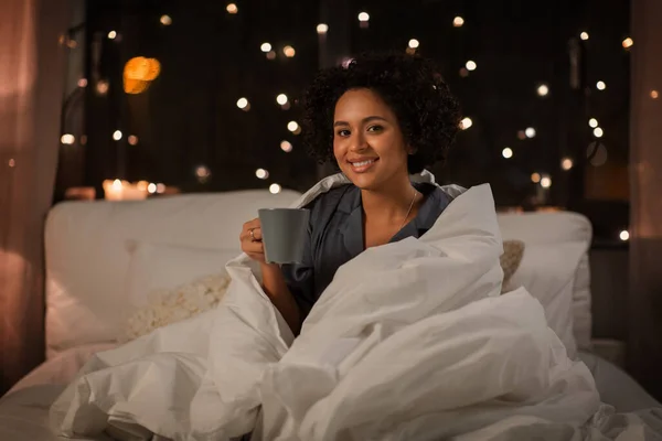 一个快乐的女人，晚上躺在床上喝咖啡 — 图库照片