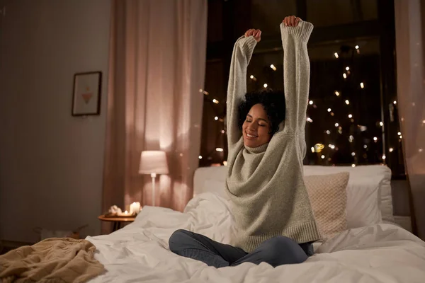 Mujer en suéter estirándose en la cama por la noche —  Fotos de Stock