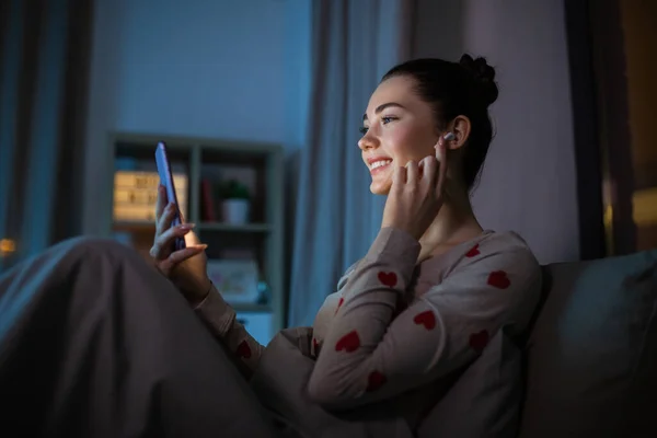 Adolescente con teléfono y auriculares en la cama por la noche — Foto de Stock