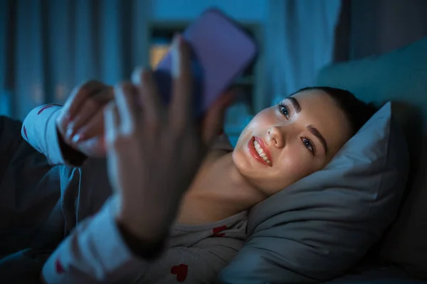 Adolescente avec téléphone couché dans le lit la nuit — Photo