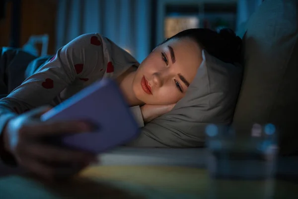 Dospívající dívka s telefonem ležící v posteli v noci — Stock fotografie