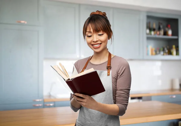 穿着围裙笑着的女人读烹调书 — 图库照片