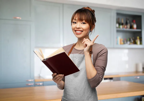 Donna sorridente in grembiule con libro di cucina aperto — Foto Stock