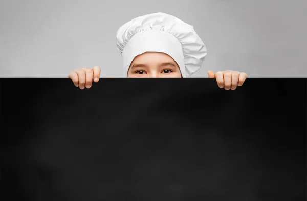 little boy in chefs toque behind black chalkboard