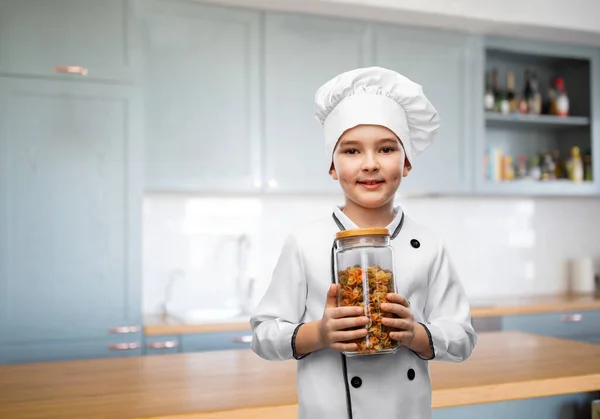 Menino sorridente em chefs toque segurando frasco com macarrão — Fotografia de Stock