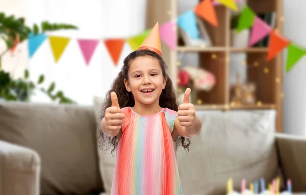 Menina feliz em chapéu de festa de aniversário mostrando polegares para cima — Fotografia de Stock