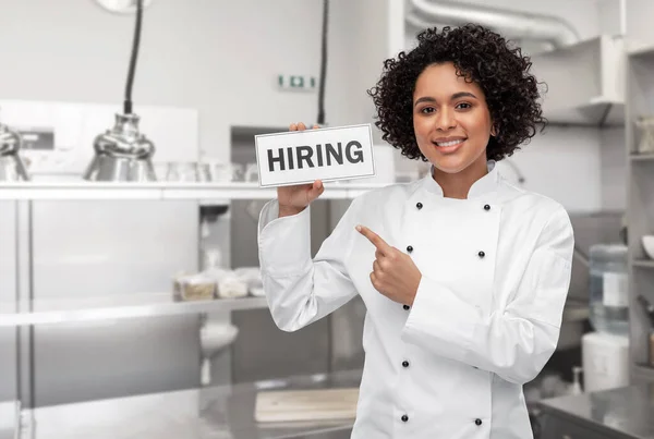 Mujer chef sonriente sosteniendo letrero de contratación en la cocina —  Fotos de Stock