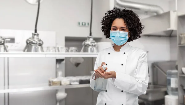 Vrouwelijke chef-kok in masker met de hand ontsmettingsmiddel op keuken — Stockfoto