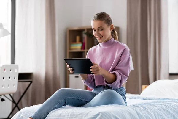 Chica sonriente con tablet pc sentado en la cama en casa —  Fotos de Stock