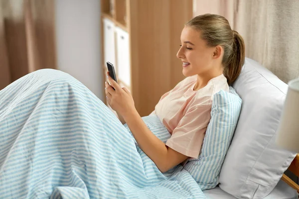 Glad flicka med smartphone i sängen hemma — Stockfoto