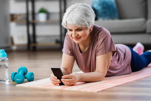Ηλικιωμένη γυναίκα με άσκηση smartphone στο σπίτι — Φωτογραφία Αρχείου