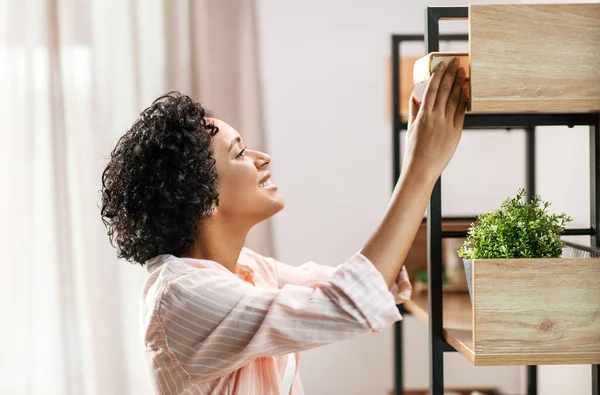 Mujer sonriente organizando libros sobre estanterías en casa —  Fotos de Stock