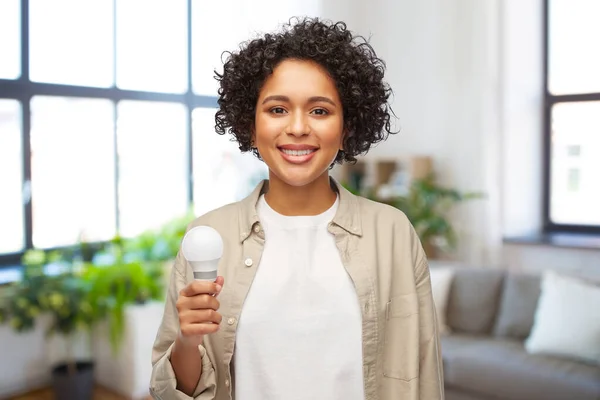 Улыбающаяся женщина держит лампочку дома — стоковое фото