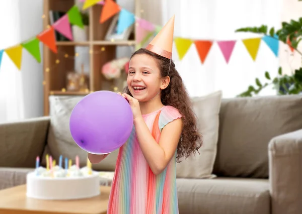 Menina feliz no chapéu de festa de aniversário soprando balão — Fotografia de Stock