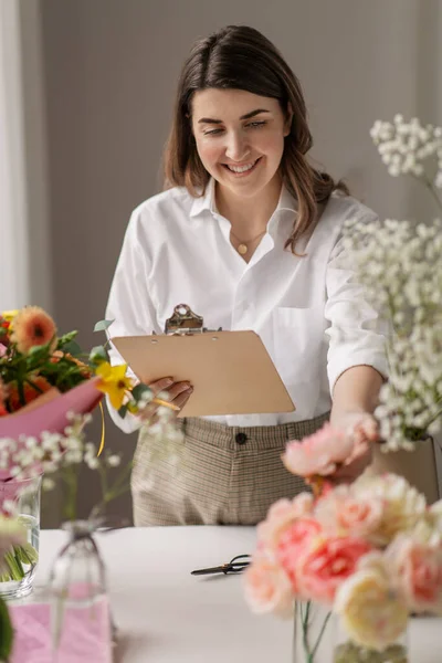 Femme heureuse avec presse-papiers et fleurs au studio — Photo