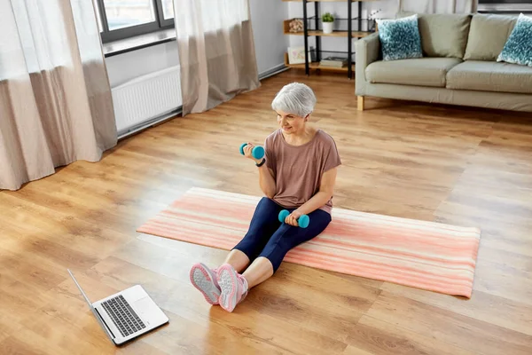 Femme avec ordinateur portable et haltères exercice à la maison — Photo