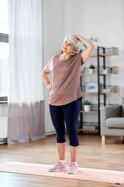 Mujer mayor sonriente haciendo ejercicio en la alfombra en casa — Foto de Stock