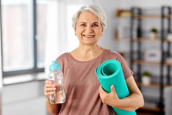 Старшая женщина с ковриком для йоги и бутылкой воды — стоковое фото