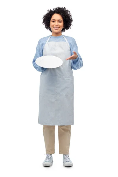 Smiling woman in apron holding clean empty plate — Stock Photo, Image